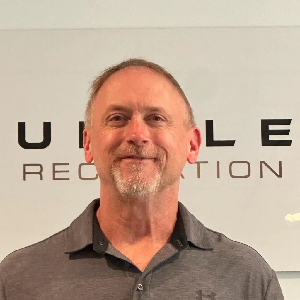 Head-and-shoulders portrait of a man in a dark polo shirt in front of a height-measurement backdrop.